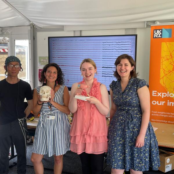 group photo of four people with a large monitor and posters behind