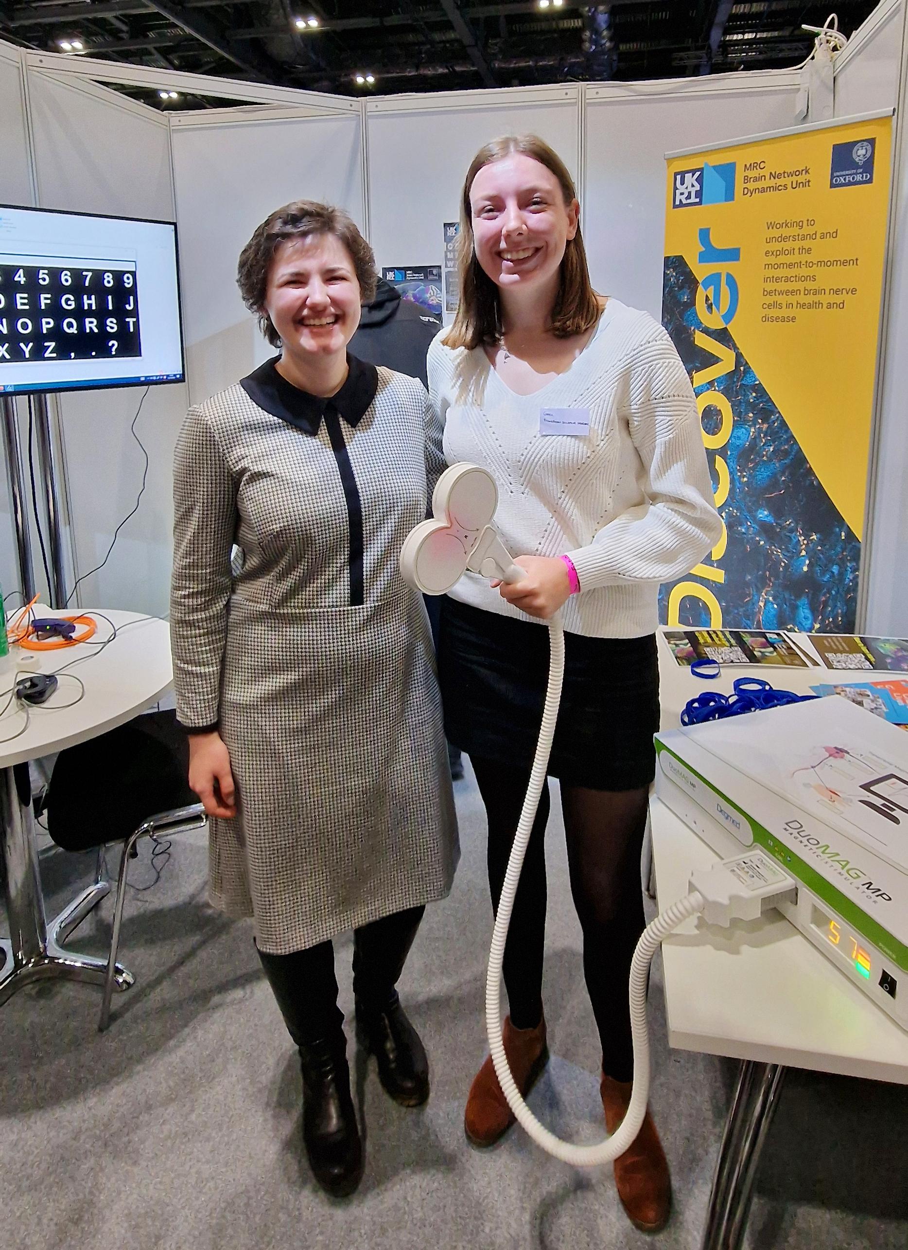 Photo of two women, one holding a TMS wand connected by a thick wire to a large machine