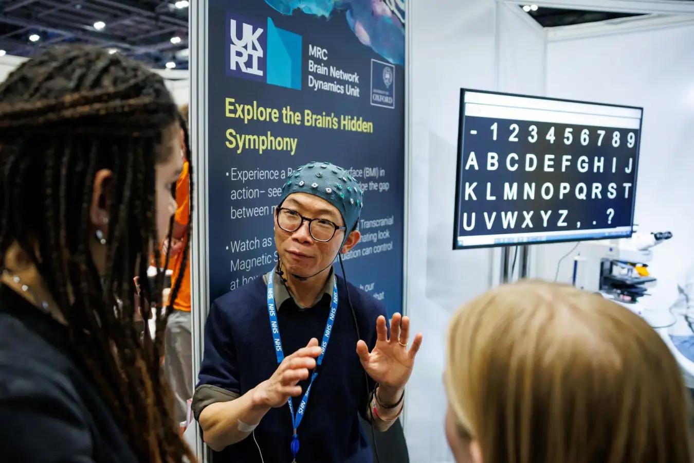 A man with an EEG cap on explains to two people listening.