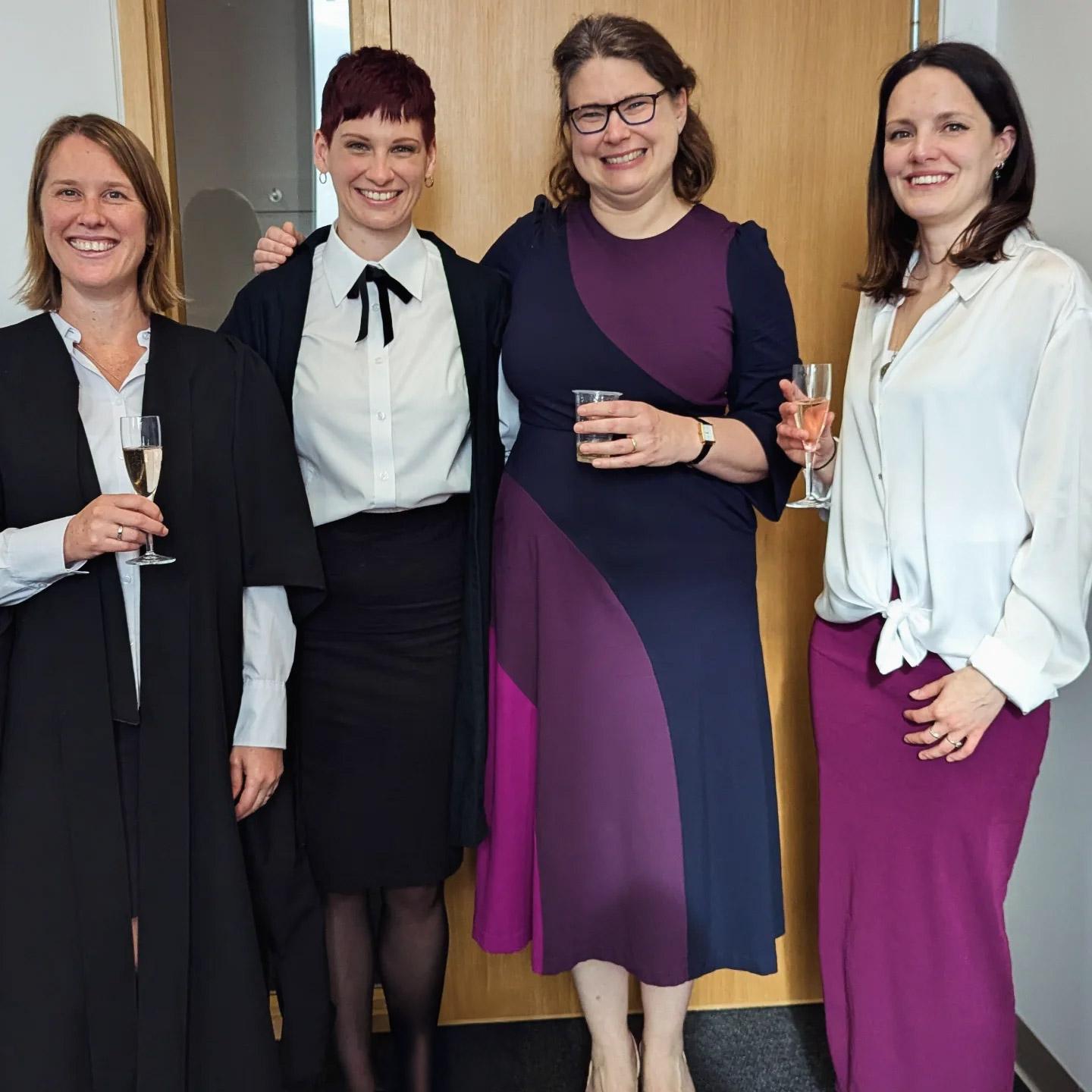 Four women standing in a row. To the left of centre, Camille wears sub fusc.