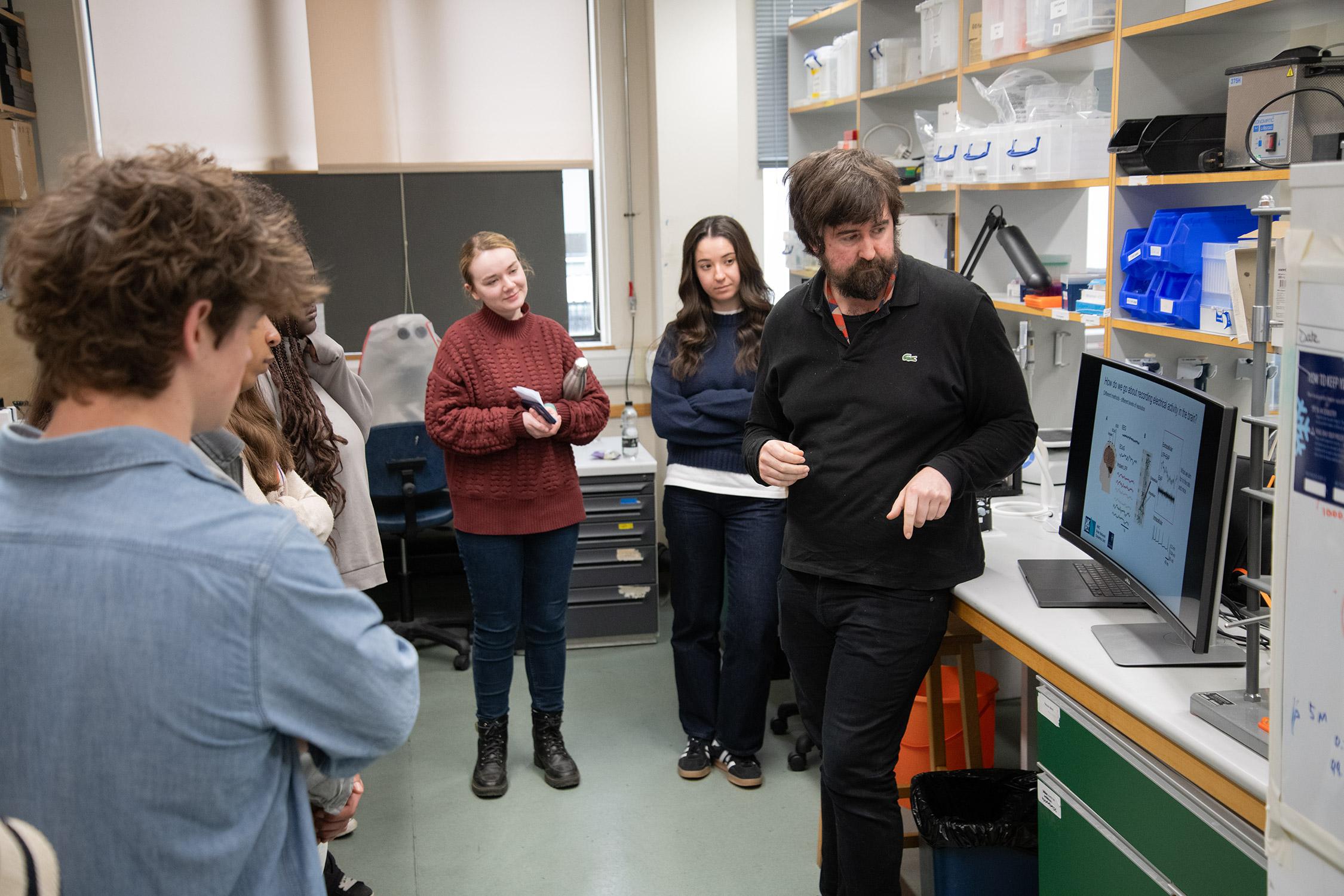 Photo of BNDU researcher Brook Perry talking with visiting pupils in a laboratory