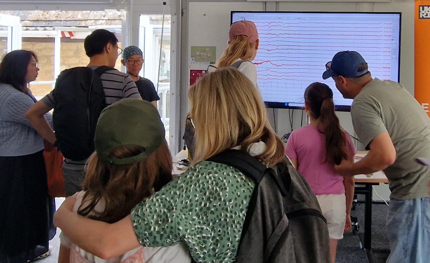 a crowd of keen young people and their parents take in the display on a large monitor of eeg output from the scientist's brain