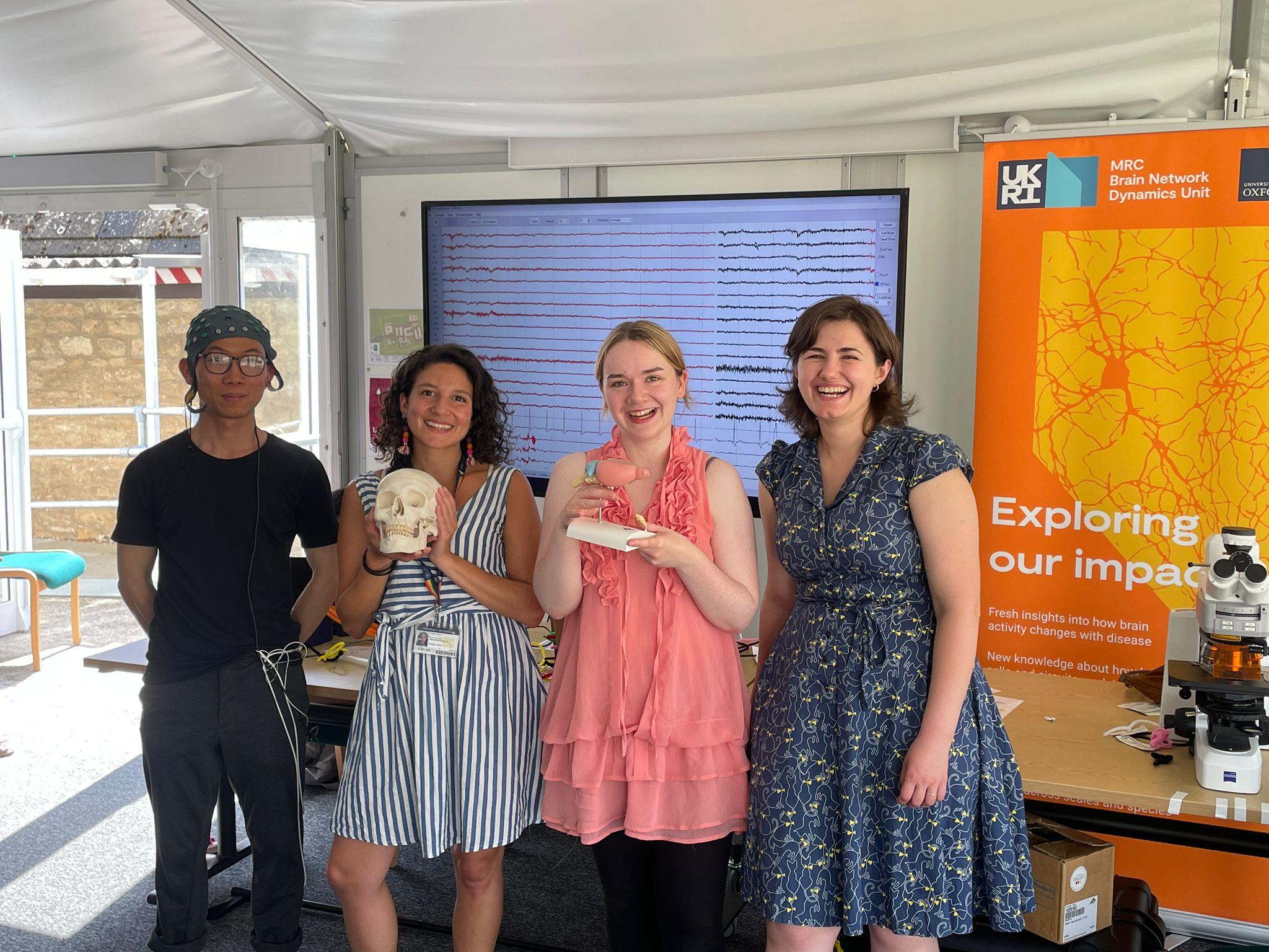 group photo of four people with a large monitor and posters behind