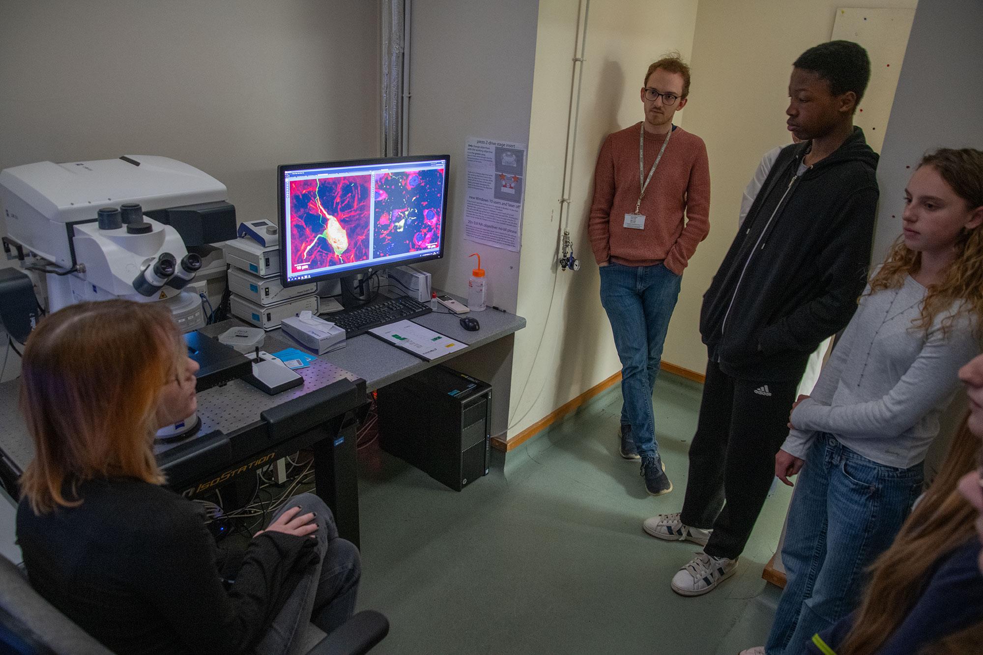 a researcher shows a computer screen with images, alongside the confocal microscope, to pupils