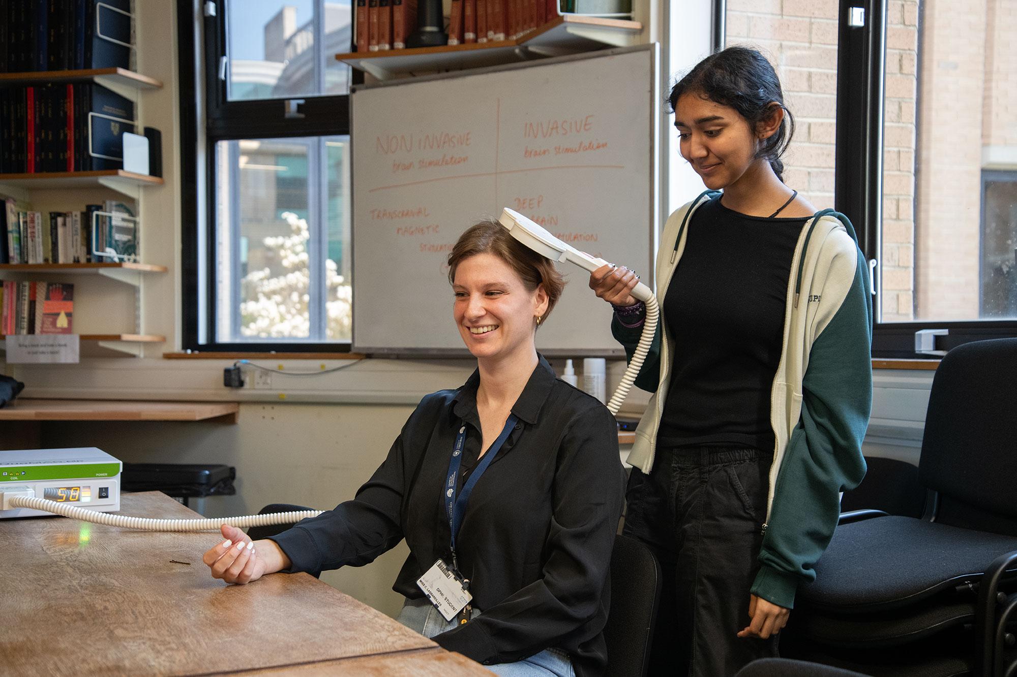 a student holds a TMS handset over the head of a researcher, who is holding out their hand